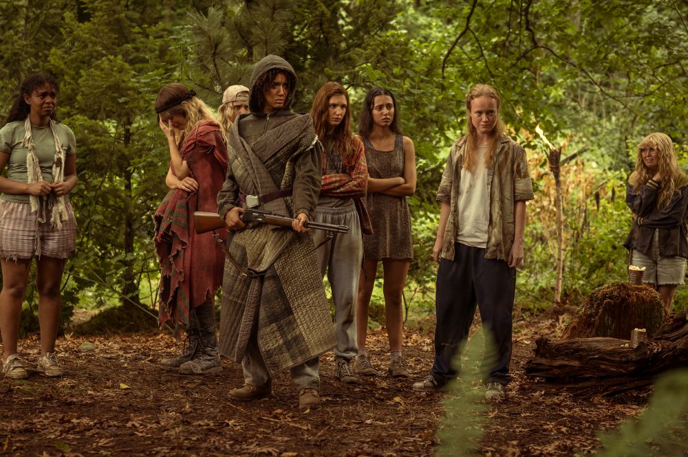 A group of teens wear mismatched, dirty clothing while holding weapons and standing in the woods during the day. They look ready to fight in Yellowjackets Season 3.