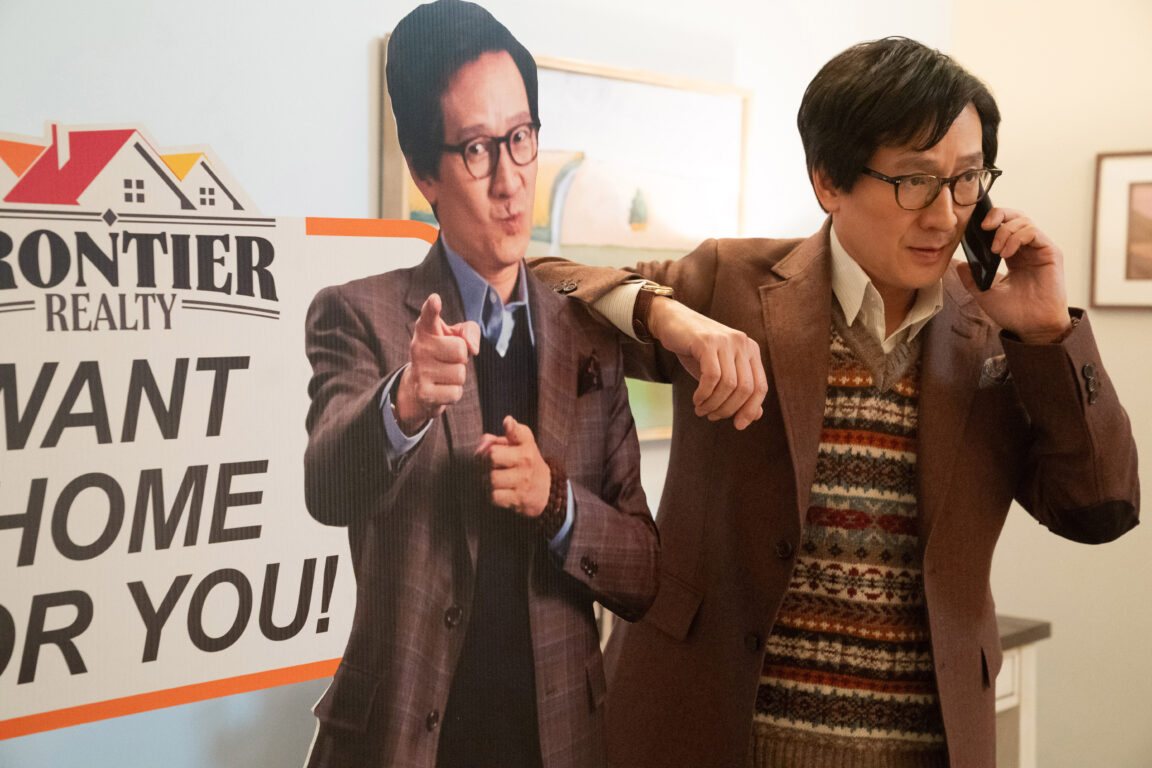 Ke Huy Quan leans on a cardboard cutout of himself pointing at the camera as he talks on the phone in the film Love Hurts.
