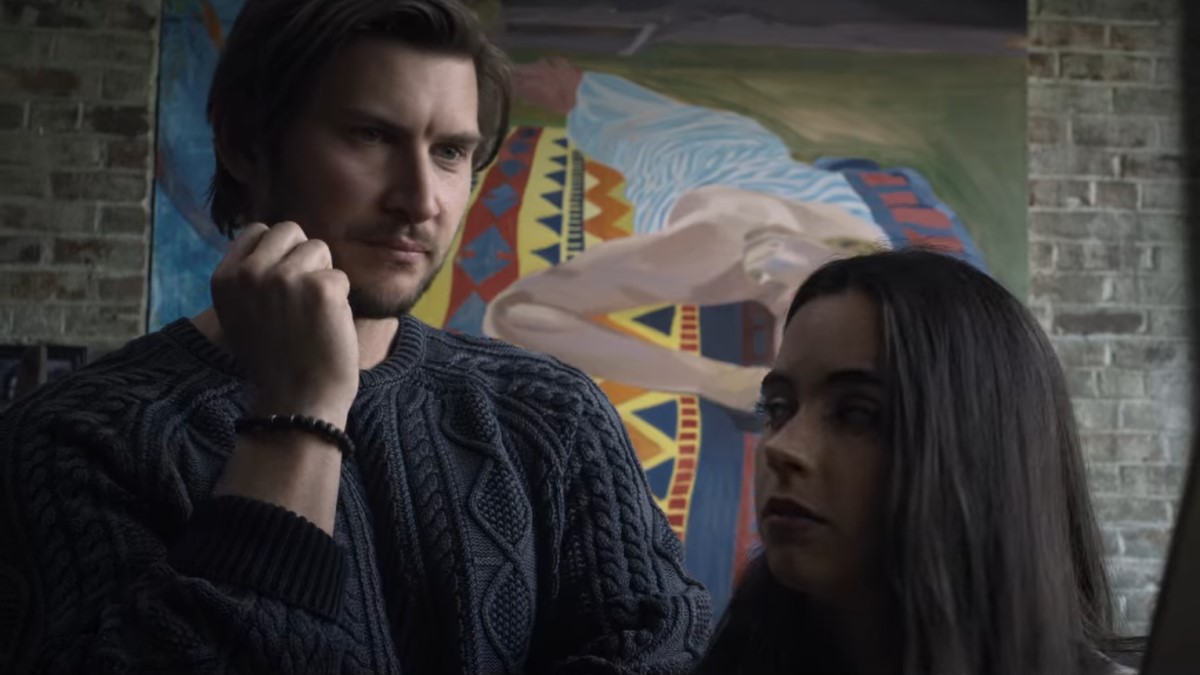 Paulo Bonetto considers the art on Maddie Redfield's easel, his face leaning on his right hand. A large painting decorates the wall in the background