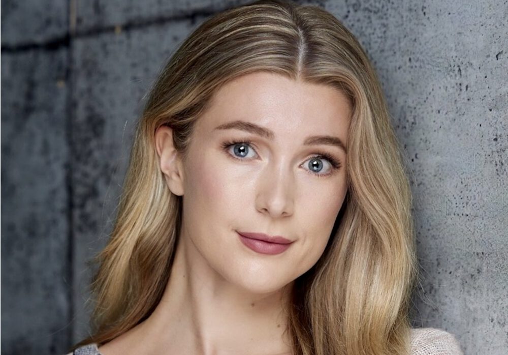 Actress Charlot Daysh, a young white woman with blonde hair, poses for a professional headshot in front of a gray background.
