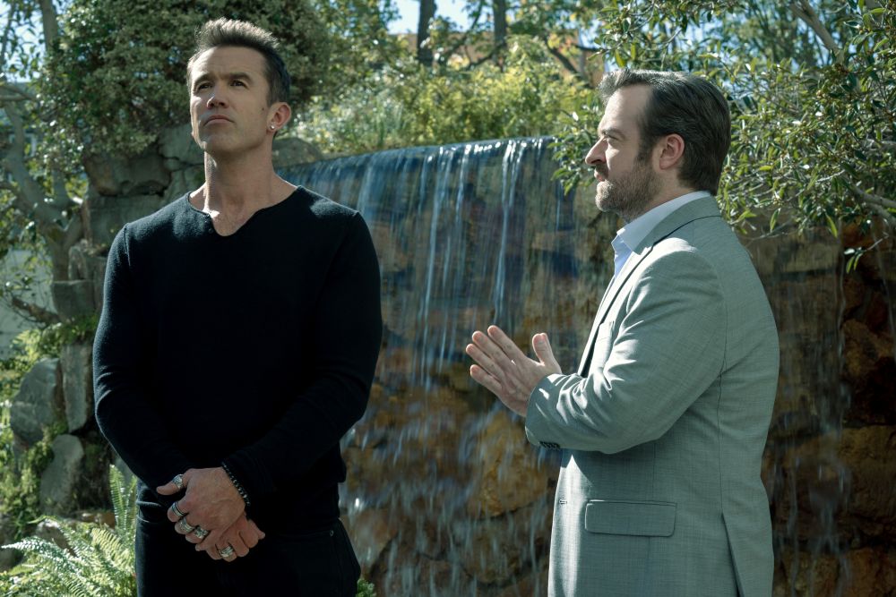 Ian and Phil stand outside on a sunny day in Japan while preparing for a video game presentation on Side Quest Season 1 Episode 1, "Song and Dance."