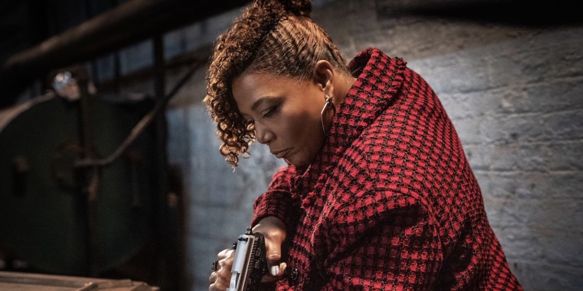 Queen Latifah holding a gun while looking down and wearing a red flannel shirt on The Equalizer Season 5 Episode 10, "Dirty Sexy Money."