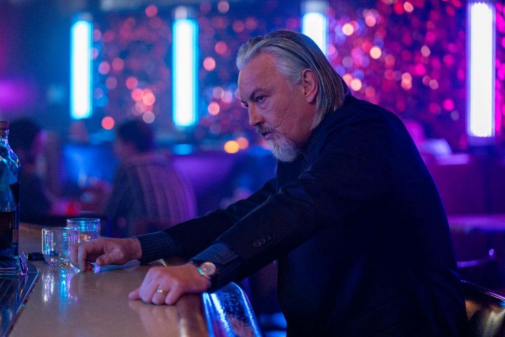 Tommy Flanagan as Walter Flynn in Power Book. He wears a suit while standing in a dimly lit bar with his hands on the bar top.