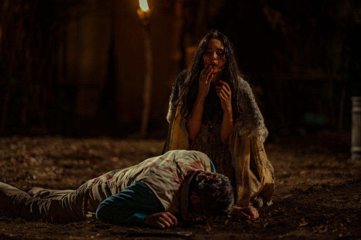 Lottie smears blood on her face while kneeling before a dead body in the woods at night on Yellowjackets Season 3 Episode 7, "Croak."