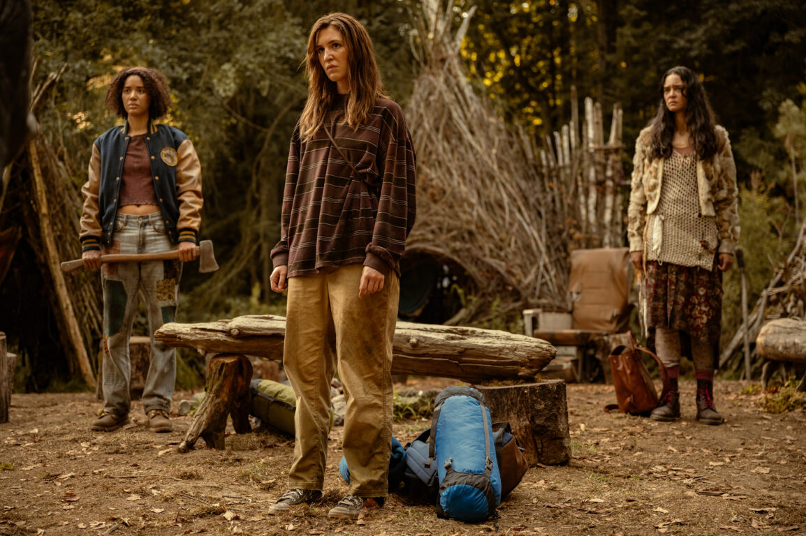 Shauna, Taissa and Lottie stand in their makeshift village in the woods during the day on Yellowjackets Season 3 Episode 9, "How the Story Ends."