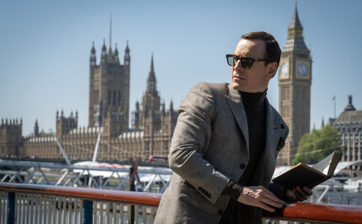 Michael Fassbender wears sunglasses as he looks over his shoulder. Big Ben is seen behind him in the film Black Bag.