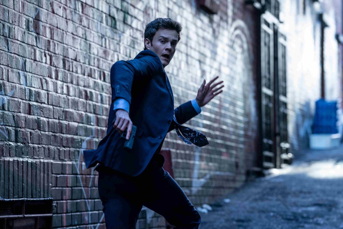 Nate (Jack Quaid) runs down an alley with a gun in Novocaine