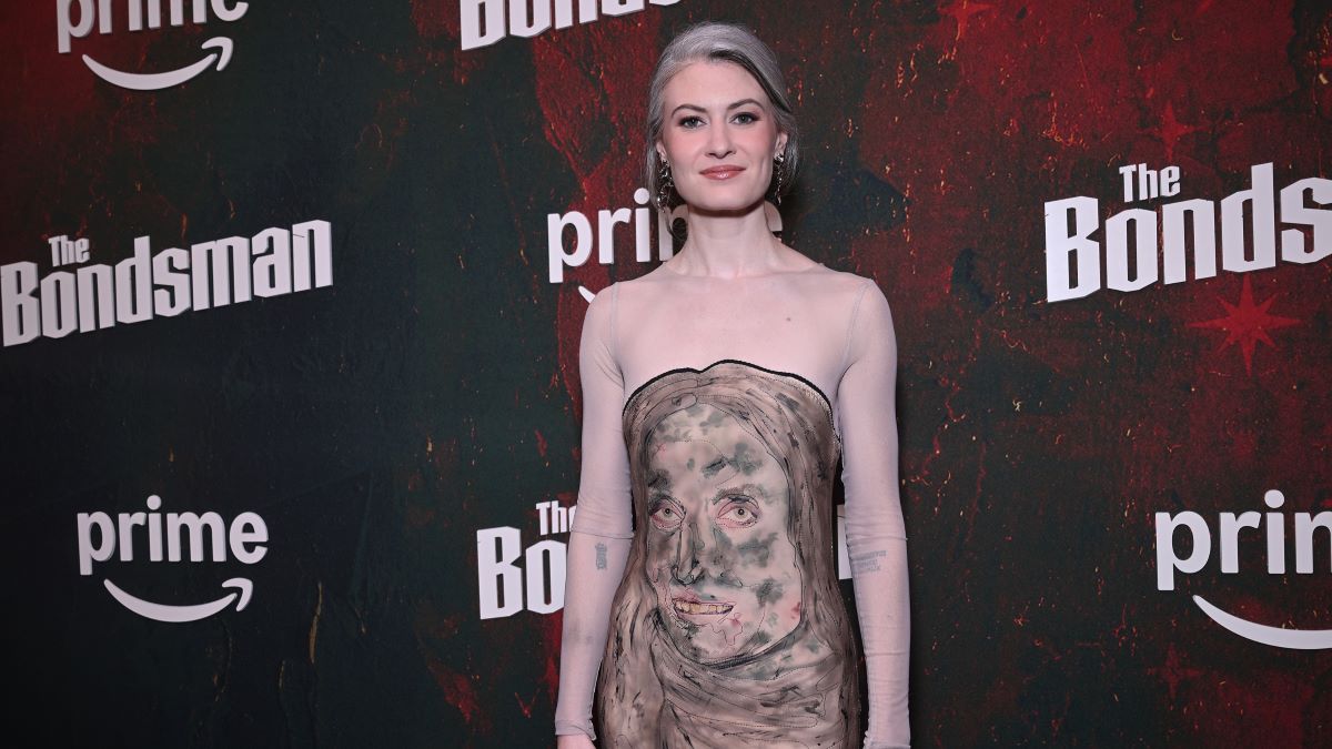 Red carpet photo of Kathrine Barnes at the premiere event for Prime Video's The Bondsman. She wears a dress with a woman's face depicted on the bodice in flesh and gray tones.