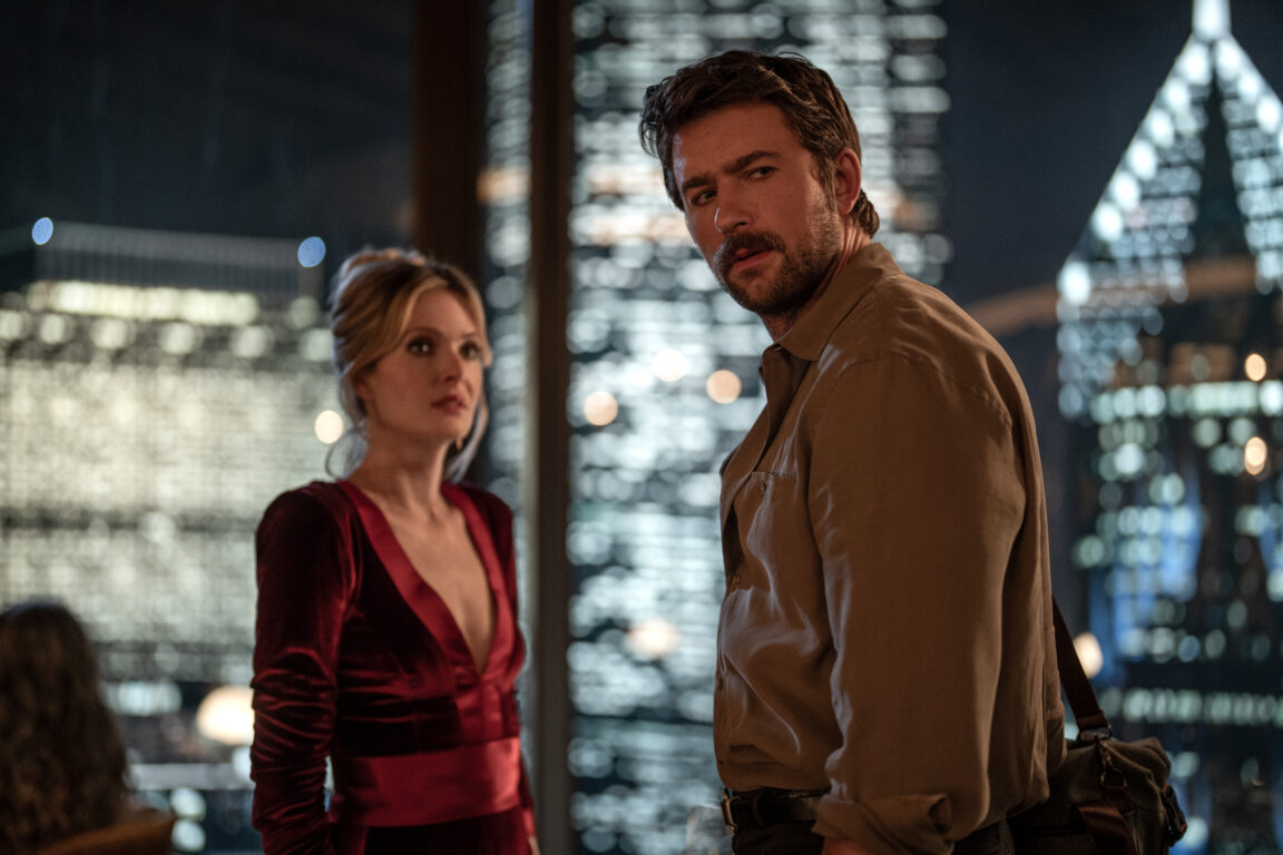 Meghann Fahy and Brandon Sklenar stand in front of an ornate glass window and look at the camera in a photo from the movie Drop.
