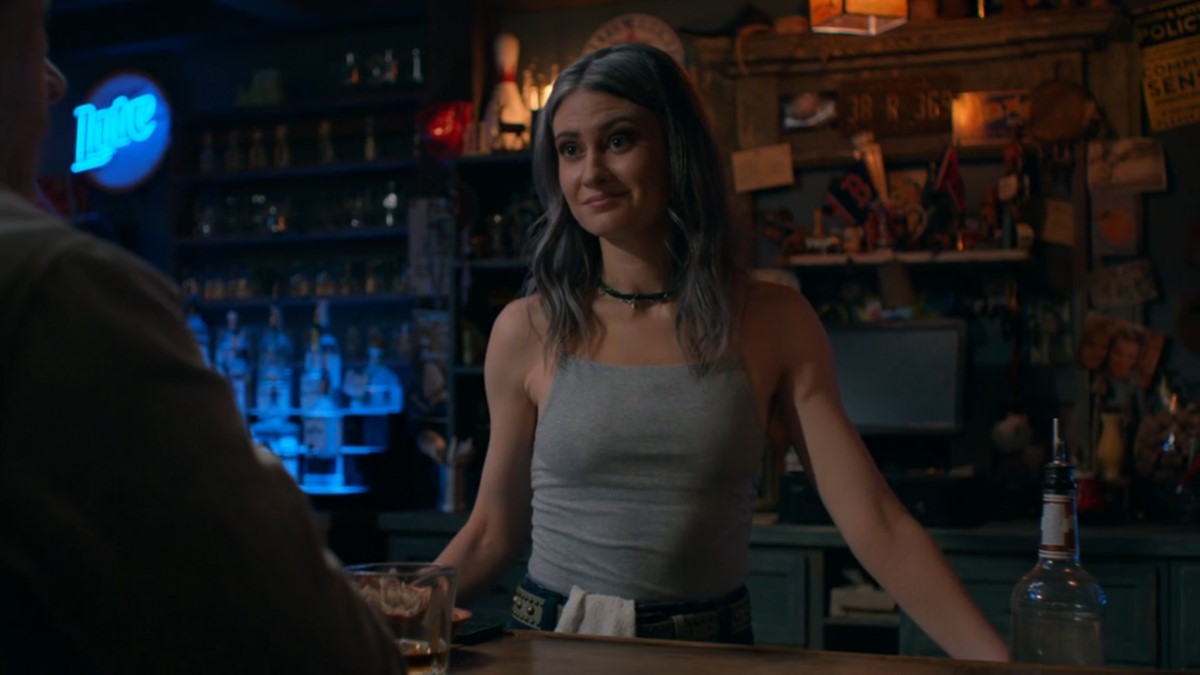 Cheryl Dawson stands behind the bar at The Boxcar wearing a gray tank top and choker necklace. She has a dishcloth tucked into her waistband.