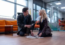Conrad and Ruby Sunday smile at each other while kneeling on the floor of an office, a pile of papers between them, on Doctor Who Season 2 Episode 4, "Lucky Day."