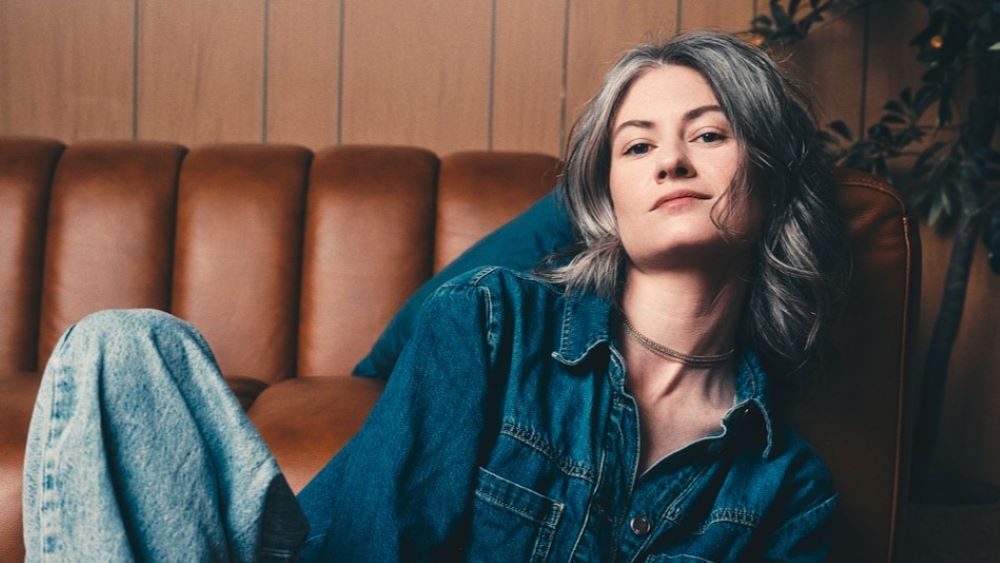 Kathrine Barnes posed casually in a blue denim shirt on a brown vinyl couch.