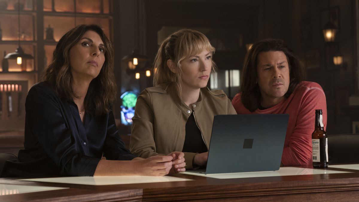 Sophie, Parker, and Eliot sit at the HQ counter, a laptop open in front of Parker. Sophie's in a dark tailored suit, Park in a tan jacket over a black top and Eliot wears a faded red henley shirt in Leverage: Redemption.