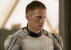 Alexander Skarsgård wears an off-white and silver-colored robot suit without a helmet. He stands at attention while looking focused in the TV series Murderbot.