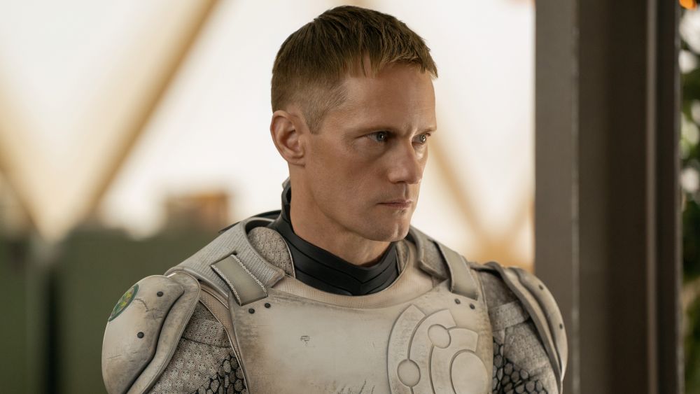 Alexander Skarsgård wears an off-white and silver-colored robot suit without a helmet. He stands at attention while looking focused in the TV series Murderbot.