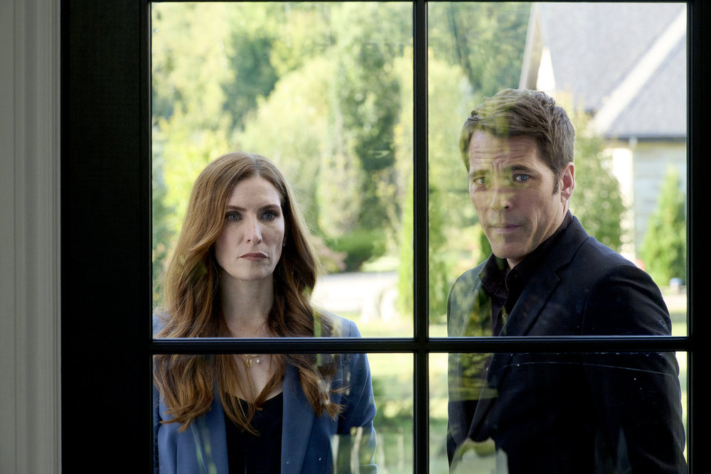 Susan and Luke stand outside a house during a sunny day while looking through a window on SurrealEstate Season 3 Episode 2, "Night Terrors."