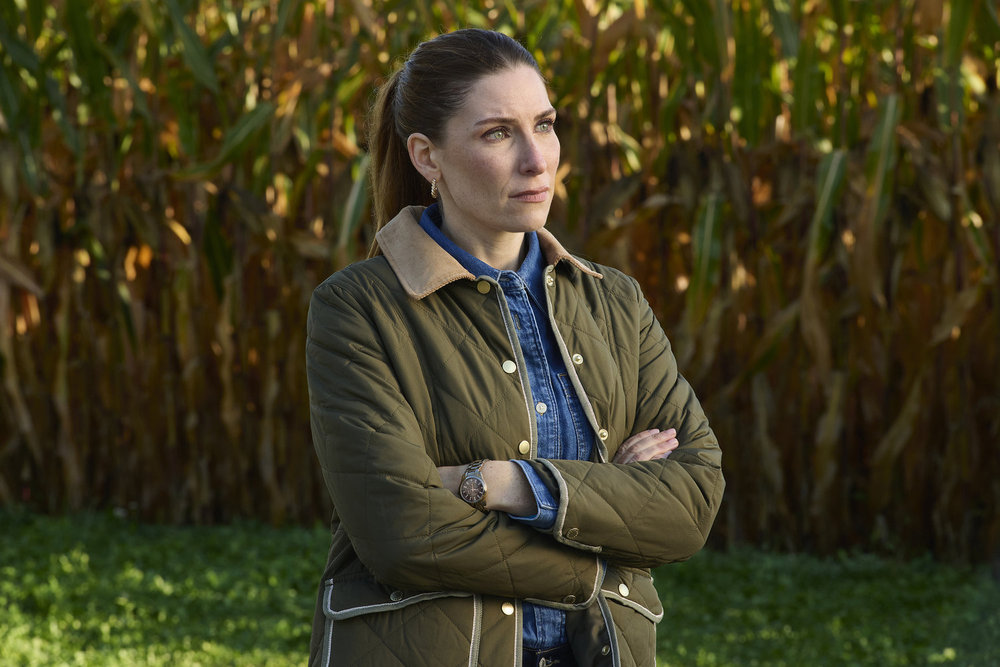 Susan crosses her arms while standing on a farm in crisp weather clothing on SurrealEstate Season 3 Episode 3, "Death Does a Refi."