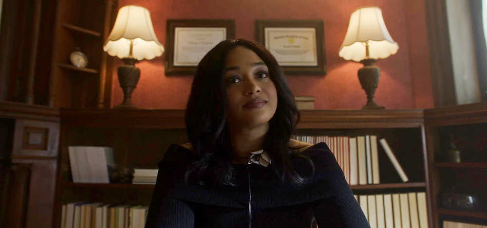 Zooey sits at her desk in a law office. She wears a black blouse and looks intently at someone out of frame on SurrealEstate Season 3 Episode 4, "A Family Thing."