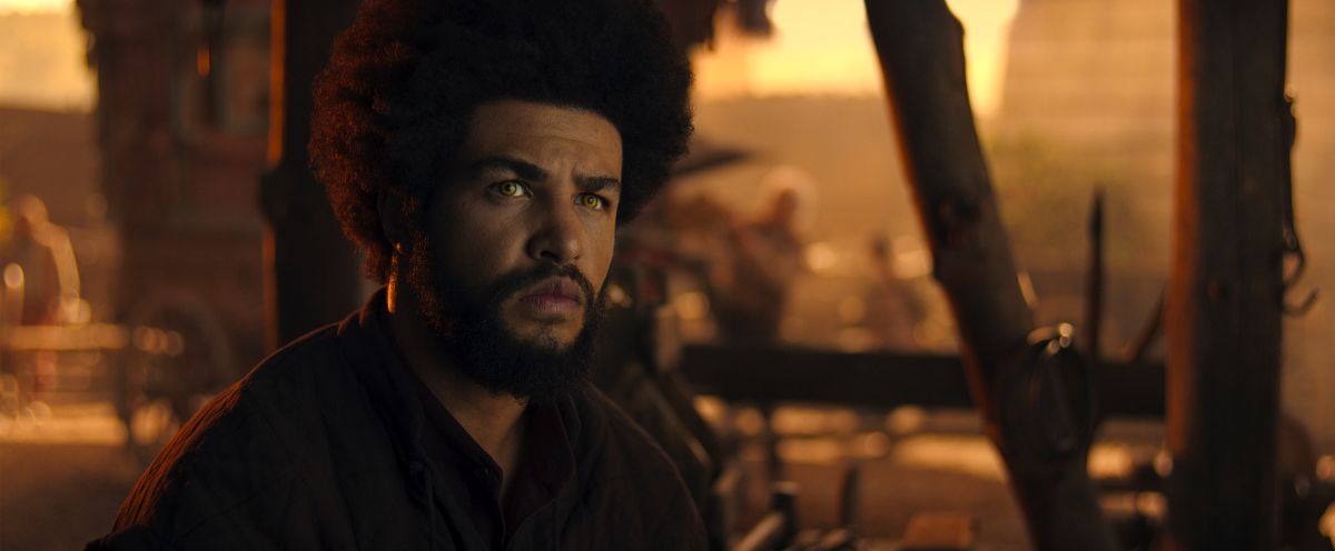 Marcus Rutherford as Perrin Aybara on The Wheel of Time Season 3 Episode 7, "Goldeneyes." Perrin sits in his forge while looking off-screen with a somber expression, his golden eyes glowing.
