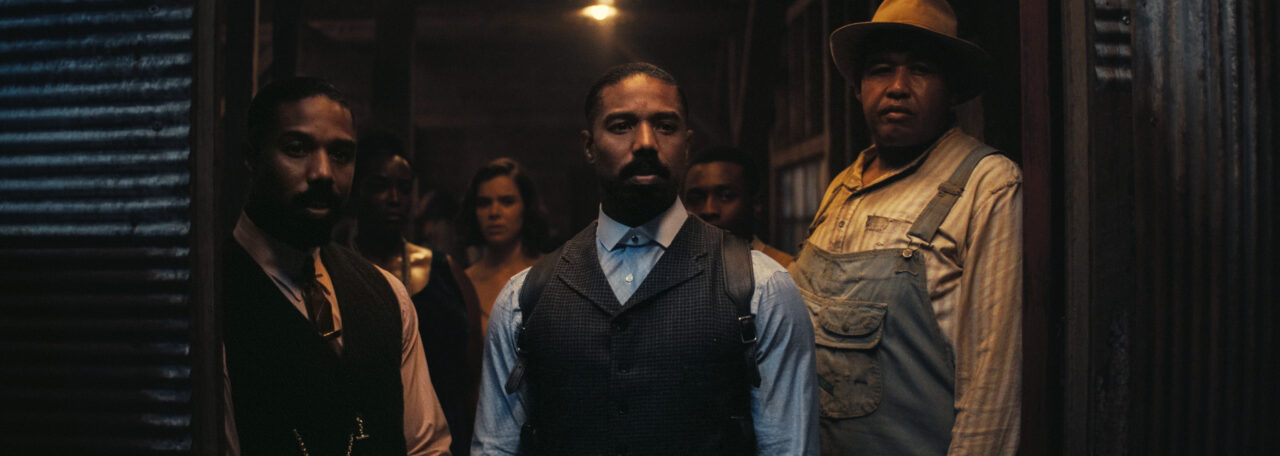 Michael B. Jordan and the cast of Sinners look through a doorway with concern in a dark room.
