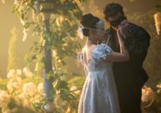 Sophie Baek wears a silver dress with a matching eye mask and dances with Benedict Bridgerton, who wears a black suit with a matching eye mask. They're at a lavish ball. Benedict kisses Sophie's hand.