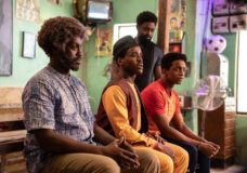 Omo, the Doctor and Amaka sit on a bench while Tunde stands behind them. They're all in a barbershop in Lagos on Doctor Who Season 2 Episode 5, "The Story & the Engine."