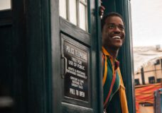 The Doctor smiles while poking his head out of the TARDIS.