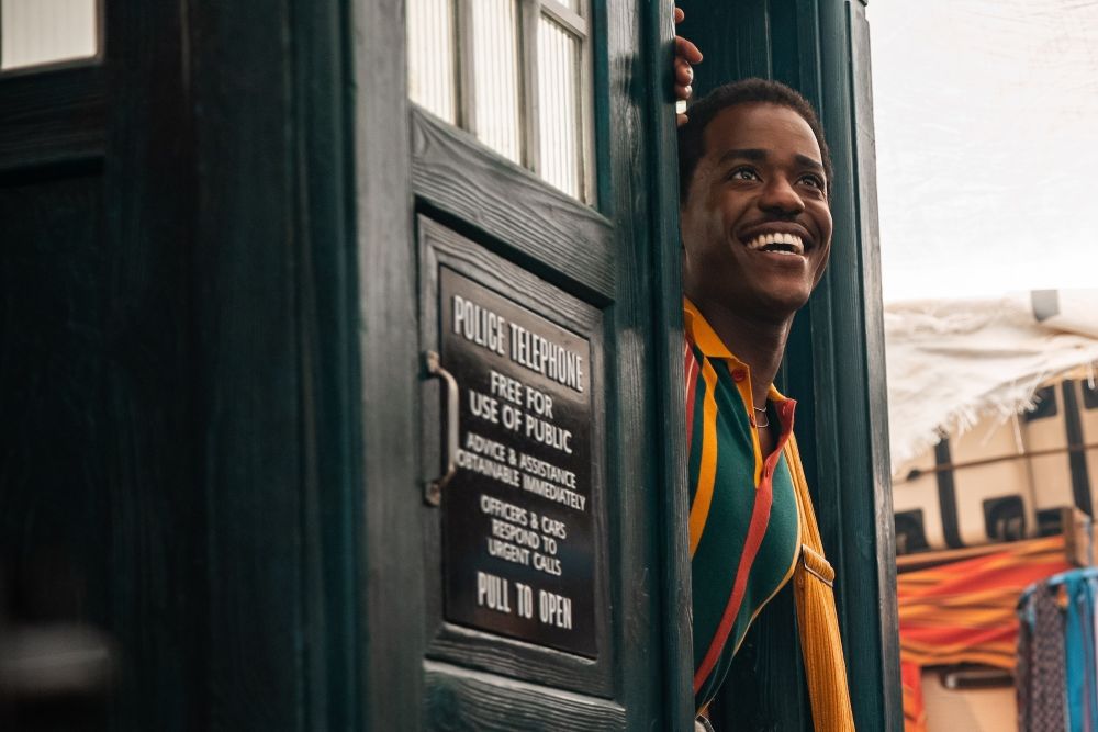 The Doctor smiles while poking his head out of the TARDIS.