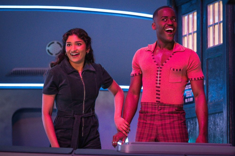 Belinda and the Doctor hold hands while standing outside the TARDIS and grinning on Doctor Who Season 2 Episode 6, "The Interstellar Song Contest."