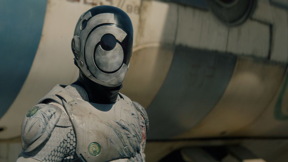 A SecUnit with its helmet on and matching armor stands alert outside a hopper on Murderbot Season 1 Episode 1, "FreeCommerce."