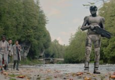 Mensah, Arada and Pin-Lee walk some distance behind Murderbot, which is in it's armor and holds a weapon. They all walk through a creek in a wooded area on an alien planet on Murderbot Season 1 Episode 3, "Risk Assessment."