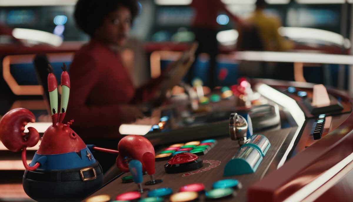 Mr. Krabs in the foreground and Uhura in the background on the bridge of the Patrick Starship Enterprise in the Star Trek: Strange New Worlds and SpongeBob SquarePants advertisement.