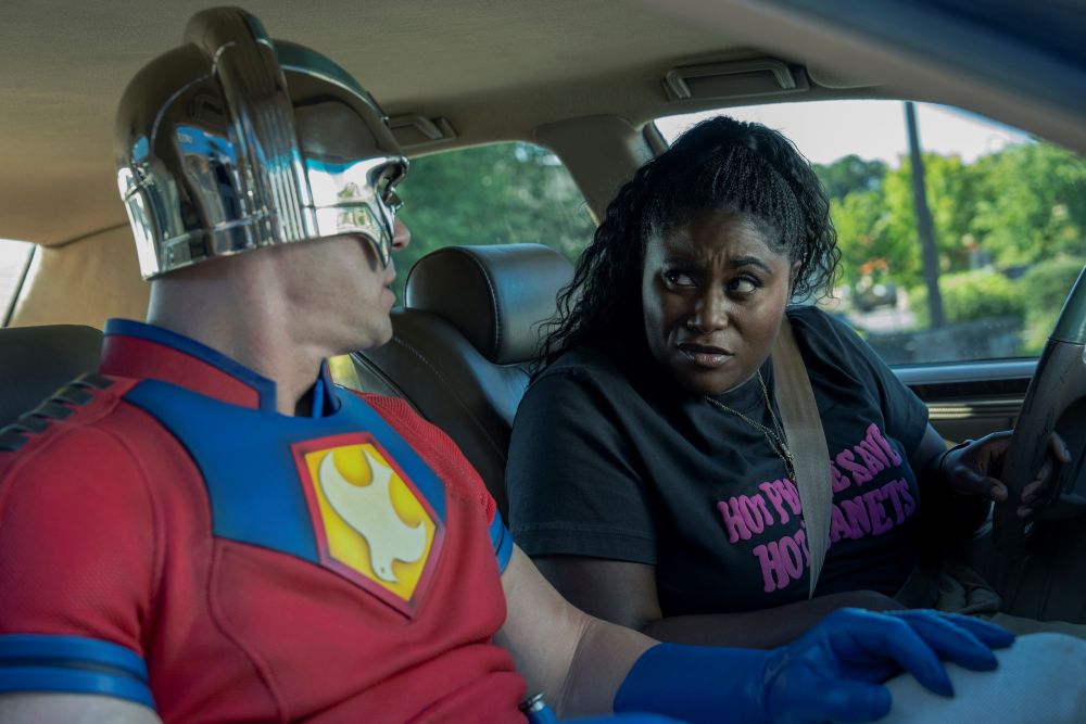 Christopher Smith wears his Peacemaker costume while sitting in the front passenger seat of the vehicle Leota Adebayo drives. Leota looks at him encouragingly.