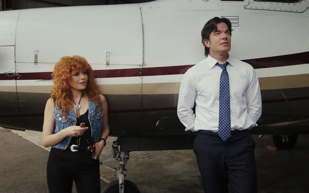 Charlie and Danny lean against the side of a private plane while chatting on Poker Face Season 2 Episode 3, "Whack-a-Mole."