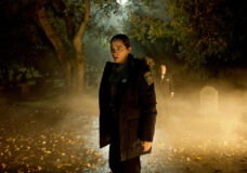 Dana Cypress wears a police uniform while standing outside at night. Fog surrounds her in the TV series Revival.