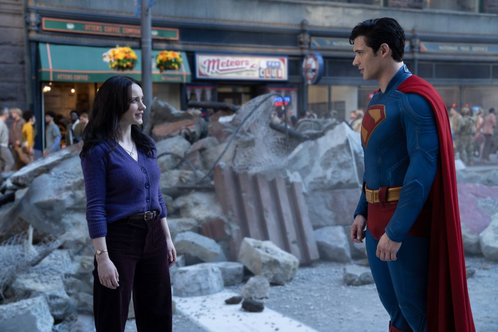 Lois Lane and Superman stand among the rubble in an outdoor shopping center during the day. Lois looks annoyed.