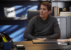 Luke sits at his desk in his office in the real estate agency while looking intently at someone out of frame on SurrealEstate Season 3 Episode 6, "Battleground."