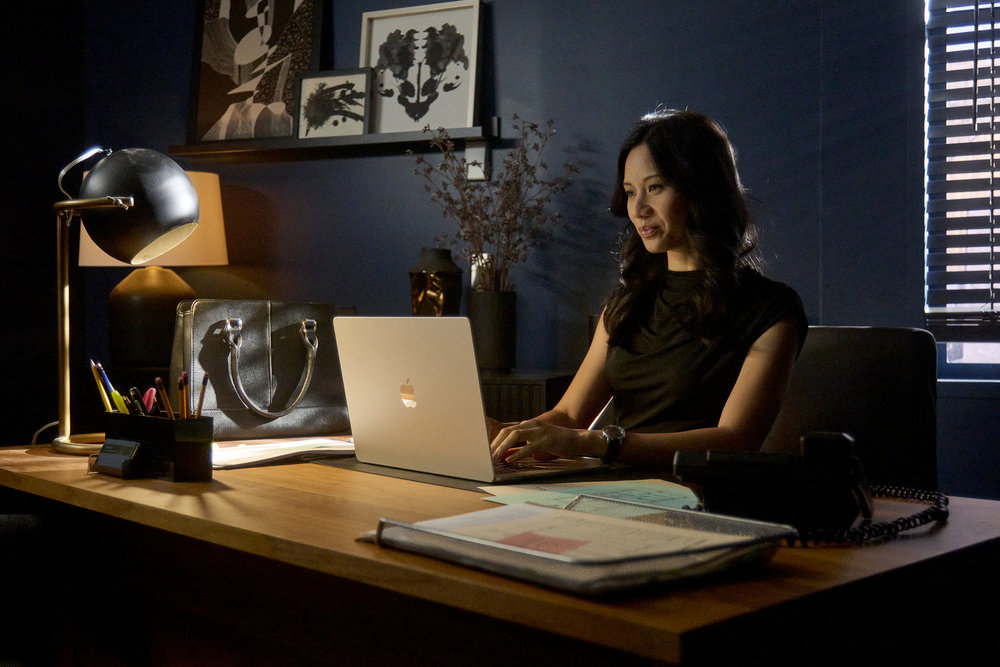 Lomax sits at her desk while typing on her laptop and smiling on SurrealEstate Season 3 Episode 7, "A Slice of Afterlife."
