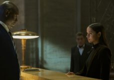 Eve stands at the counter of the Continental. Charon addresses her. In the background, Winston stands in the shadows in a still from the film From the World of John Wick: Ballerina.
