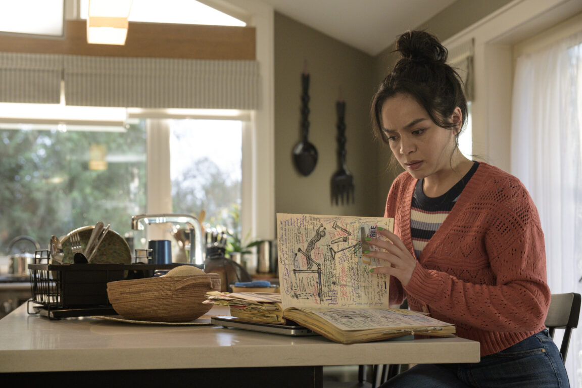 Stefani (Kaitlyn Santa Juana) tries to read Iris' notes while sitting in a brightly lit kitchen island.