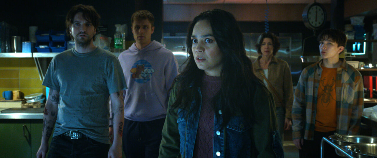 Stefani Reyes and her pals stand in a dimly lit room while looking shocked in the horror film Final Destination: Bloodlines.
