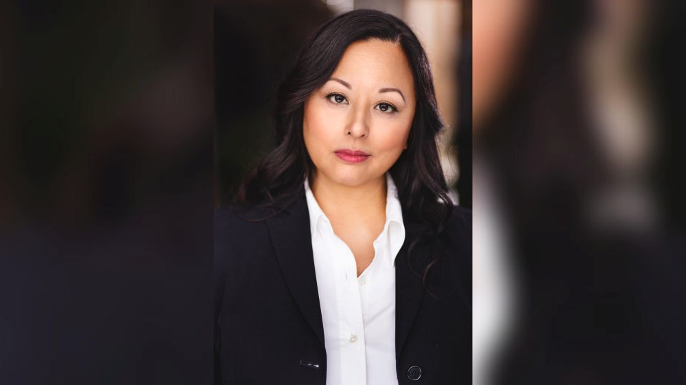 Actress Jane Luk wears a black blazer with a white button-down top while posing for a headshot.