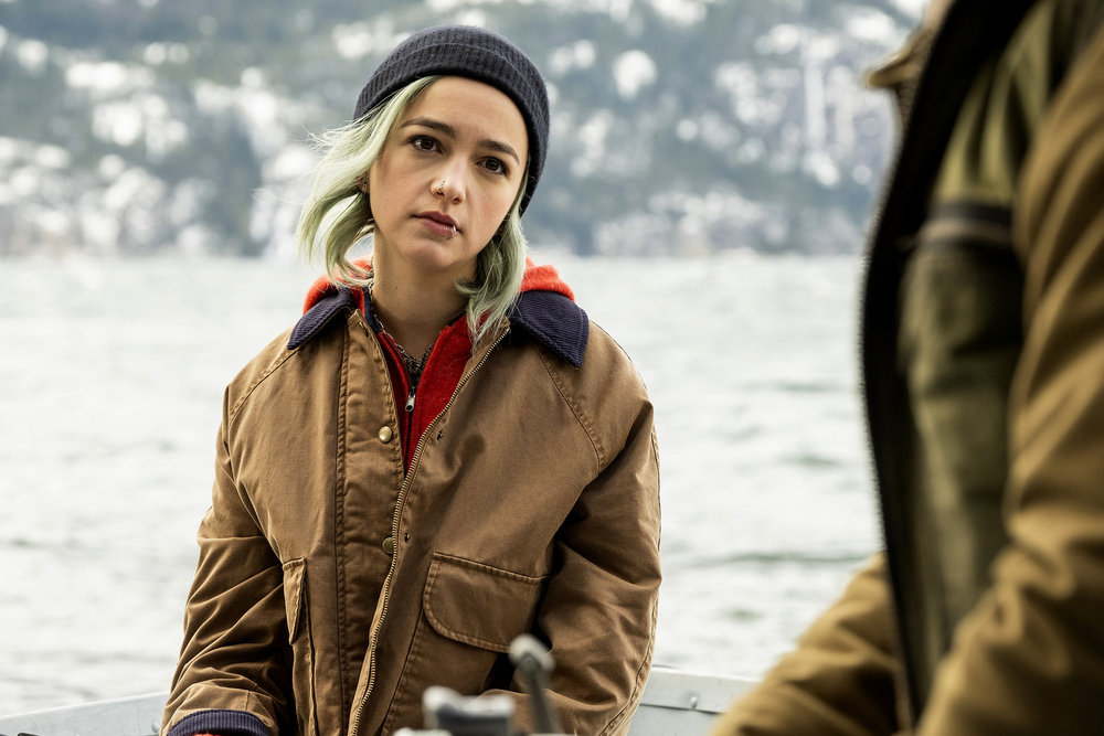Liza Vanderspeigle sits in a boat on the lake while wearing a Carhartt coat and a beanie on Resident Alien Season 4 Episode 5, "The Human Condition."