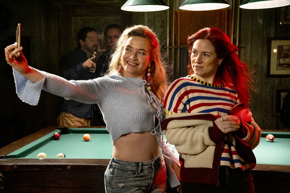 Judy holds a phone up for a selfie while standing beside D'arcy in the dimly lit bar on Resident Alien Season 4 Episode 6, "Soul Providers."