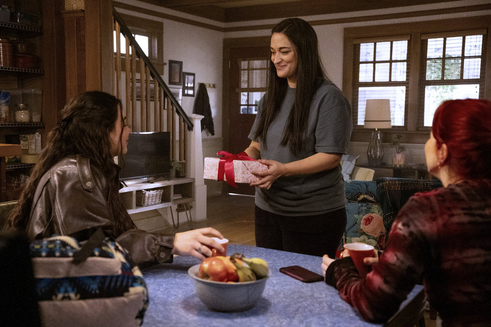 Asta gives Jay a gift while the latter sits at the dining room table in Asta's and D'arcy's house on Resident Alien Season 4 Episode 10, "The End Is Here."